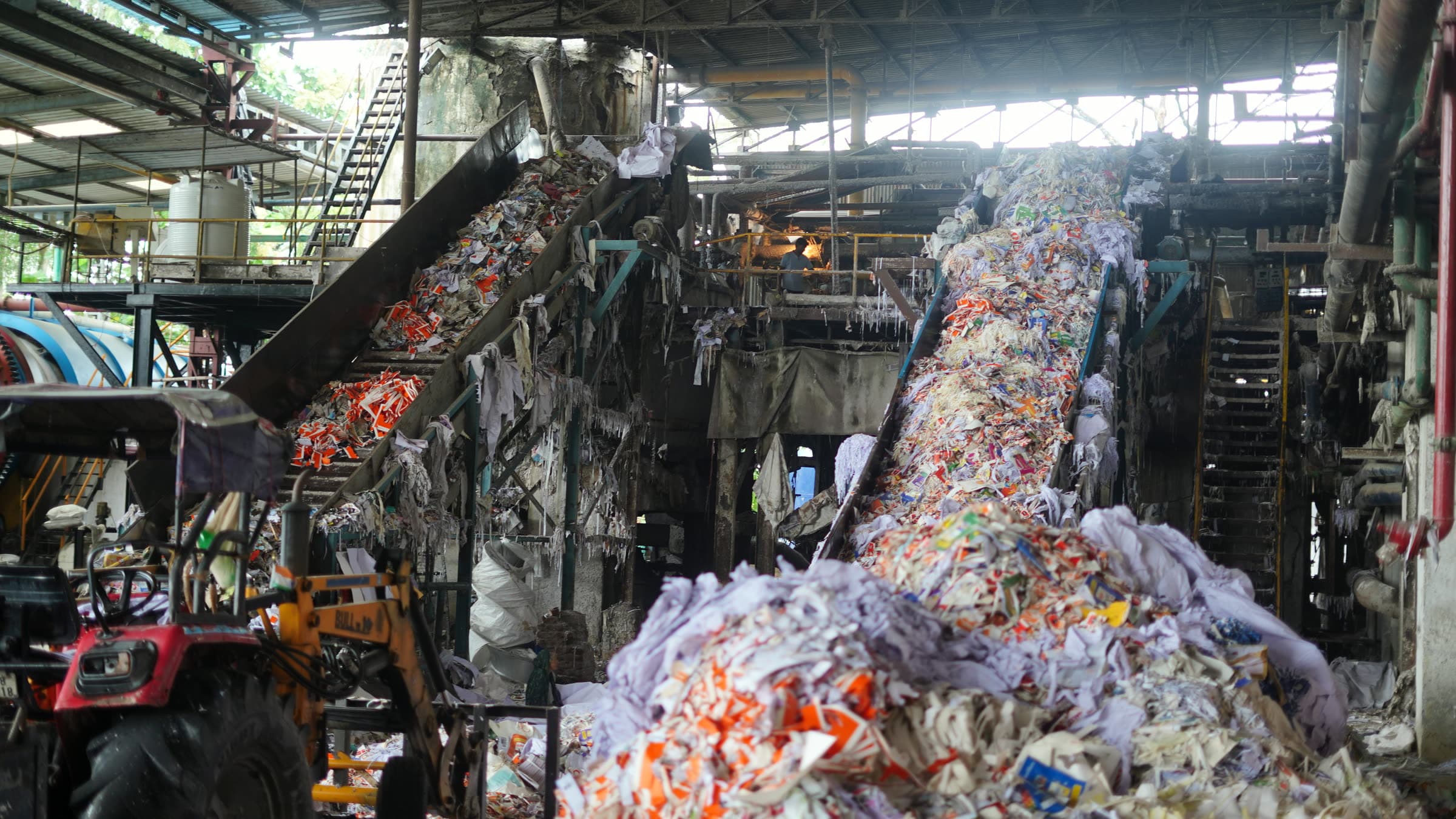 Loader at the foot of the feed conveyor, sorted stock climbing towards the pulping line